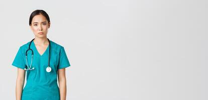 covid19, gezondheidszorg arbeiders, pandemisch concept. uitgeput jong Aziatisch vrouw verpleegster, dokter op zoek moe na verschuiving in ziekenhuis, op zoek verdrietig met vermoeidheid, staand wit achtergrond in scrubs foto