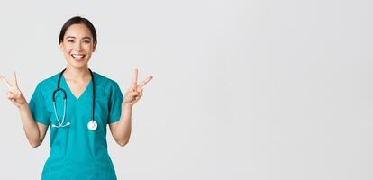 covid19, gezondheidszorg arbeiders, pandemisch concept. gelukkig Aziatisch vrouw dokter, verpleegster in scrubs tonen vrede kawaii gebaar en lachend, blijven positief gedurende werk in ziekenhuis, wit achtergrond foto