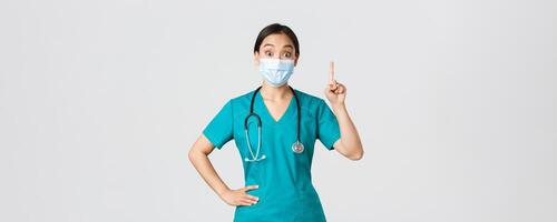 covid19, coronavirus ziekte, gezondheidszorg arbeiders concept. opgewonden Aziatisch vrouw dokter, arts in medisch masker en scrubs hebben suggestie, verhogen inhoudsopgave vinger eureka gebaar, wit achtergrond foto