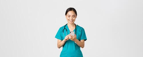 covid19, gezondheidszorg arbeiders en voorkomen virus concept. glimlachen gelukkig mooi Aziatisch vrouw intern, dokter maken telefoon telefoongesprek, op zoek Bij mobiel telefoon scherm verheugd, berichten of gebruik makend van app foto
