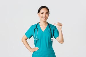 covid19, gezondheidszorg arbeiders, pandemisch concept. professioneel zelfverzekerd vrouw Aziatisch dokter, verpleegster in scrubs richten Bij haarzelf en lachend, garantie ze weet wat doen, wit achtergrond foto