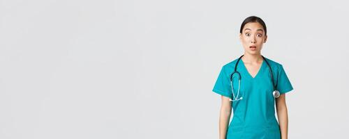 covid19, gezondheidszorg arbeiders, pandemisch concept. onder de indruk en verrast Aziatisch verpleegster in scrubs laten vallen kaak en staren Bij camera sprakeloos, op zoek versteld staan over- wit achtergrond foto