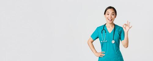 covid19, gezondheidszorg arbeiders, pandemisch concept. verrast en gelukkig Aziatisch vrouw dokter, verpleegster in scrubs tonen Oke gebaar en glimlachen versteld staan, lof mooi hoor werk, mee eens met iemand foto