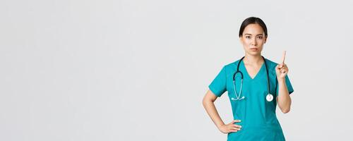 covid19, gezondheidszorg arbeiders, pandemisch concept. serieus kijkend professioneel vrouw Aziatisch dokter in schrobben, arts beven vinger in verbod, waarschuwing gebaar, verbieden iets foto