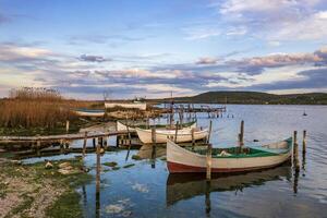 de rustig middag Aan een meer met een houten pier en boten in de kleurrijk lucht. foto