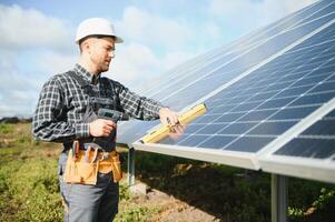 portret van glimlachen zelfverzekerd ingenieur technicus met elektrisch schroevendraaier, staand in voorkant van onvoltooid hoog buitenkant zonne- paneel foto voltaïsch systeem