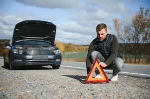 knap jong Mens met zijn auto gebroken naar beneden door de langs de weg foto