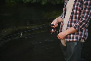 visser vangsten een forel Aan de rivier- in zomer foto