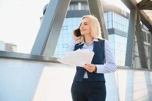 bedrijf vrouw met telefoon in de buurt kantoor. portret van mooi glimlachen vrouw in mode kantoor kleren pratend Aan telefoon terwijl staand buitenshuis. telefoon communicatie. hoog kwaliteit afbeelding. foto