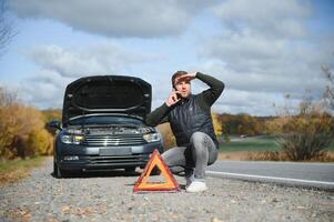 knap jong Mens met zijn auto gebroken naar beneden door de langs de weg foto