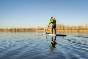 senior mannetje peddelaar is peddelen staan omhoog paddleboard Aan een kalmte meer in vroeg voorjaar landschap in Colorado foto
