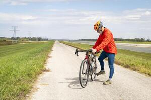 atletisch senior fietser met een grind toeren fiets Aan een dijk spoor langs keten van rotsen kanaal in de buurt graniet stad in Illinois foto