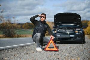 knap jong Mens met zijn auto gebroken naar beneden door de langs de weg foto