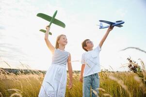 rennen jongen en meisje Holding twee groen en blauw vliegtuigen speelgoed- in de veld- gedurende zomer zonnig dag foto