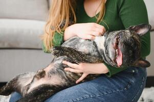 mooi meisje, glimlachen en zittend Aan verdieping in de buurt Frans bulldog foto