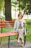 ouderen vrouw zittend en ontspannende Aan een bank buitenshuis in park foto