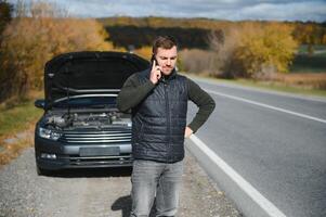 een Mens oproepen een telefoon aantal naar praten naar een monteur. de auto kapot gegaan naar beneden Aan de langs de weg. de concept voor repareren, helpen, probleem, reparatie. wazig achtergrond. foto