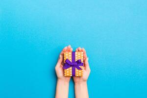 vrouw armen Holding geschenk doos met gekleurde lint Aan blauw tafel achtergrond, top visie en kopiëren ruimte voor u ontwerp foto