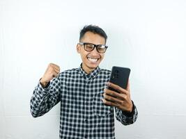 Aziatisch Mens Holding mobiel telefoon en balanceren vuist met glimlachen uitdrukking lezing bericht. foto