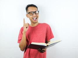 portret van glimlachen Aziatisch Mens Holding boek en richten vinger omhoog krijgen idee. foto