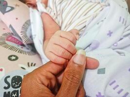 een vader Holding de hand- van een pasgeboren baby terwijl hij slaapt. foto