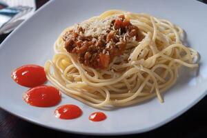 spaghetti bolognese met kaas besprenkeld is geplaatst Aan een wit bord met een houten achtergrond foto