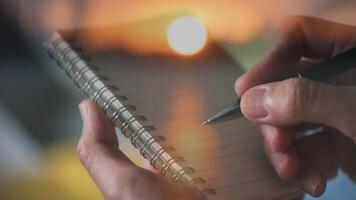 hand- houden pen schrijven Aan notitieboekje met vervagen zonsondergang achtergrond in concept van herinneringen reizen dagboek foto