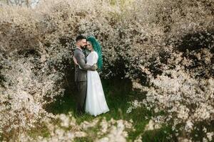 een gebaard bruidegom Toneelstukken en een meisje met groen haar- tegen de achtergrond van bloeiend voorjaar foto