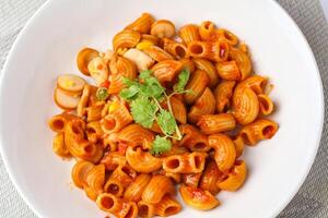 macaroni met tomaat saus en peterselie in een wit kom geserveerd Aan een wit bord, top visie foto