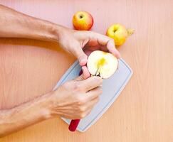dichtbij omhoog mannetje handen besnoeiing een appel in plakjes. top visie van voorbereidingen treffen fruit over- keuken tafel. foto