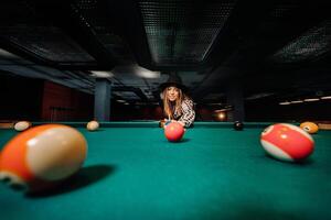 een meisje in een hoed in een biljart club met een keu in haar handen hits een bal.spelen zwembad foto