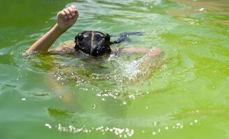 weinig meisje in de groen water van heel vuil zwembad foto