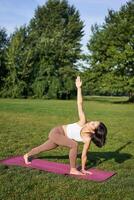 verticaal schot van jong Koreaans vrouw aan het doen yoga opleiding Aan rubber mat, maken asana opdrachten Aan vers lucht in park foto