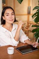 glimlachen jong vrouw Schepper, creatief meisje tekening Aan digitaal tablet met grafisch pen, drinken koffie in cafe foto