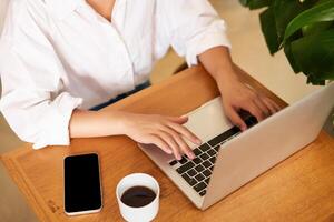 bijgesneden schot van vrouw handen typen Aan laptop toetsenbord, drinken koffie, werken in cafe, aan het studeren, aan het doen huiswerk foto