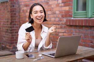 enthousiast Aziatisch meisje zittend met credit kaart en laptop, betalen contactloos, boodschappen doen online via computer foto