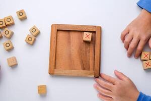 weinig broers en zussen spelen houten bord spel boter kaas en eieren Aan tafel in leven kamer. familie uitgeven tijd samen Aan weekend. foto