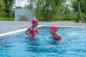 twee weinig meisjes zwemmen en spelen in water. kinderen in zwemmen zwembad hebben pret gedurende familie zomer vakantie. foto
