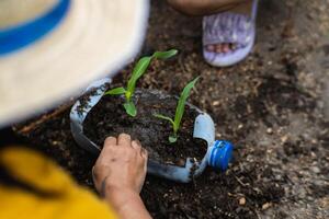 weinig meisje en mam toenemen planten in potten van gerecycled water flessen in de achtertuin. recycle water fles pot, tuinieren activiteiten voor kinderen. recycling van plastic verspilling foto