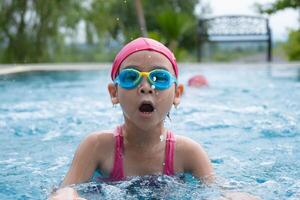 mooi weinig meisje zwemmen en spelen in water. kinderen in zwemmen zwembad hebben pret gedurende familie zomer vakantie. foto