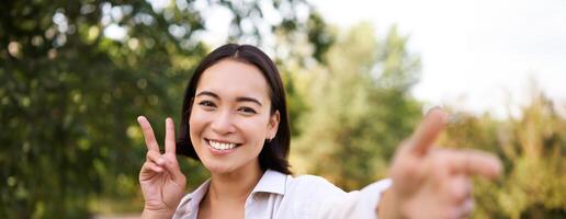 mensen en levensstijl. gelukkig Aziatisch vrouw duurt selfie in park, foto Aan smartphone, glimlachen en op zoek blij