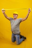 vakman arbeider met moeilijk hoed is meten met een plakband meten geïsoleerd Aan geel achtergrond foto