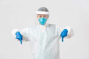 covid19, coronavirus ziekte, gezondheidszorg arbeiders concept. verrast en opgewonden vrouw dokter, arts in persoonlijk beschermend uitrusting richten vingers omlaag, staand wit achtergrond foto