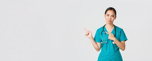 covid19, gezondheidszorg arbeiders, pandemisch concept. sceptisch en twijfelachtig Aziatisch vrouw verpleegster in scrubs richten bovenste links hoek en grimassen niet geamuseerd, niet Leuk vinden Product, wezen aarzelend foto