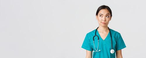 gezondheidszorg arbeiders, voorkomen virus, quarantaine campagne concept. attent Aziatisch vrouw dokter, verpleegster in scrubs op zoek bovenste links hoek en grijns onzeker, denken, wit achtergrond foto