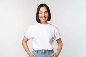 levensstijl. gelukkig modern Aziatisch meisje, glimlachen en op zoek gelukkig Bij camera, poseren in wit t-shirt en jeans, studio achtergrond foto