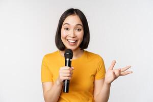 beeld van jong Aziatisch vrouw pratend in microfoon, uitvoeren met microfoon, geven toespraak, staand in geel t-shirt tegen wit achtergrond foto