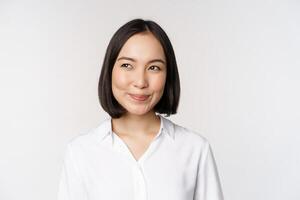 beeld van glimlachen Aziatisch vrouw planning, denken van iets, dagdromen, staand over- wit achtergrond met zelfvoldaan gezicht foto