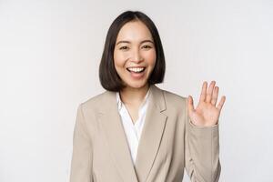 vriendelijk bedrijf vrouw, Aziatisch kantoor dame golvend hand- en gezegde Hallo, Hoi gebaar, staand over- wit achtergrond foto