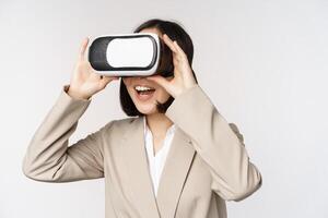 versteld staan bedrijf vrouw in pak gebruik makend van virtueel realiteit bril, op zoek versteld staan in vr koptelefoon, staand over- wit achtergrond foto